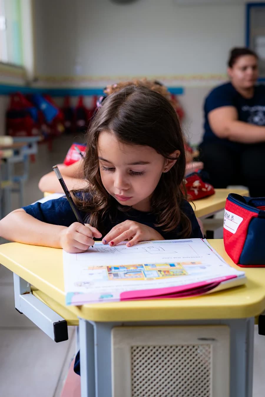 Criança concentrada escrevendo em um caderno na sala de atividades