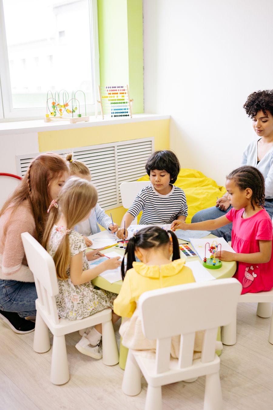 Grupo de crianças pintando juntas em uma mesa, acompanhadas por uma educadora